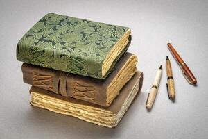 stack of retro journals with decked edge handmade paper pages and stylish pens, journaling concept photo